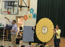  Principal addressing students and standing by prize wheel